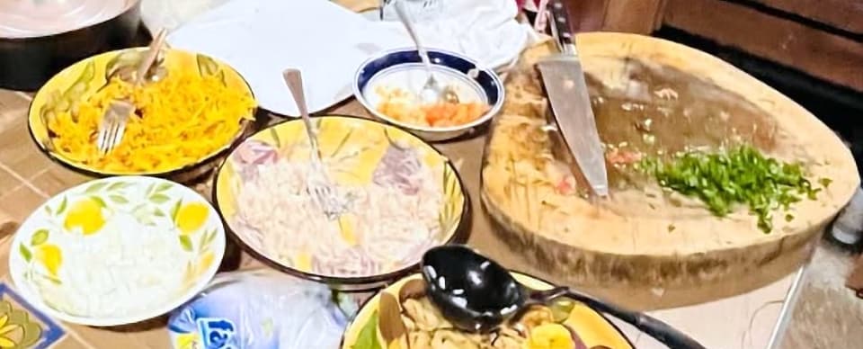 Platos caseros servidos sobre el mesón de la cocina: zanahoria rallada, ensaladas y una tabla de picar con un cuchillo y hierbas picadas.